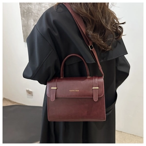 Détail du sac bandoulière bordeaux avec boucle dorée sur un trench-coat de couleur foncée