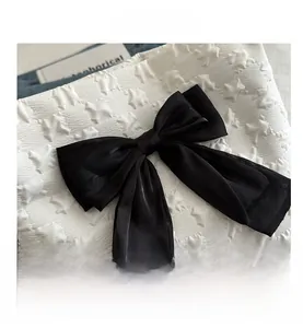 Détail d'un nœud en satin noir sur tissu blanc avec texture étoilée en relief