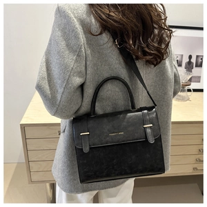 Détail d'un sac bandoulière noir avec sangle large et lettrage doré sur le rabat