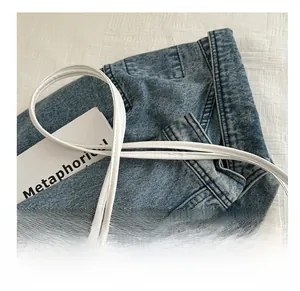 Détail de la fine bandoulière en cuir blanc sur un fond contrasté en denim bleu foncé