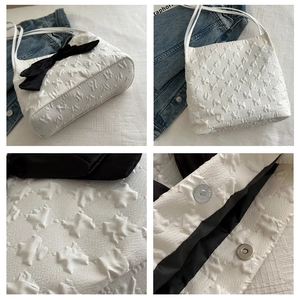 Détail d'un sac cabas en tissu blanc avec un grand nœud noir et un fermoir magnétique