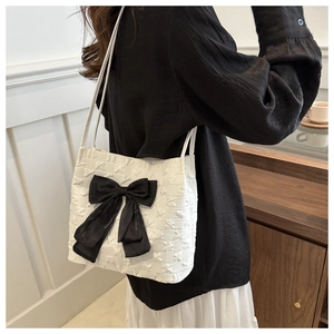 Détail du cabas blanc à texture gaufrée avec grand nœud noir porté par un modèle