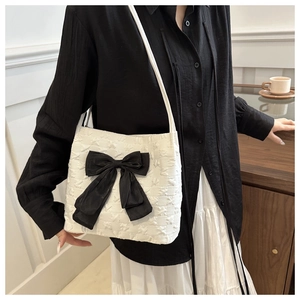 Sac fourre-tout blanc élégant avec nœud noir porté par un mannequin dans un café