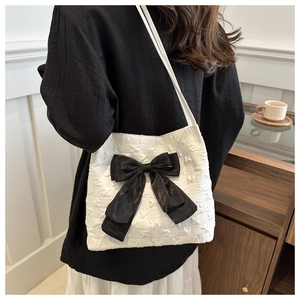 Détail du sac à bandoulière blanc texturé avec un grand nœud en satin noir