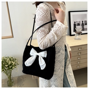Détail d'un nœud chic sur un sac cabas noir texturé porté par un mannequin en intérieur