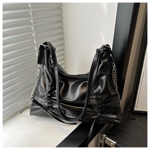 Detail of black tote bag with ruched design, silver chain strap, and matte leather texture