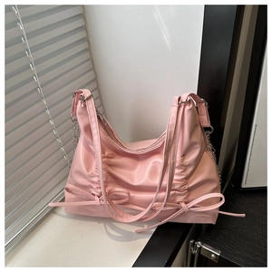 Detail of pink pleated tote with bow accents and chain strap in natural sunlight