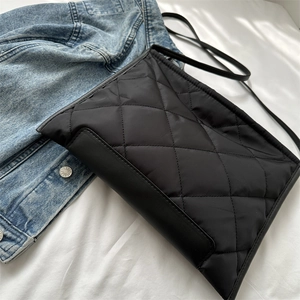 Détail d'un sac cabas noir matelassé avec passepoil en cuir sur fond de tissu épuré