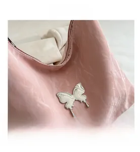 Detail of pink pleated leather tote bag featuring a silver butterfly metal ornament