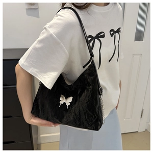 Close-up of black pleated faux leather shoulder bag with silver butterfly and chain detail