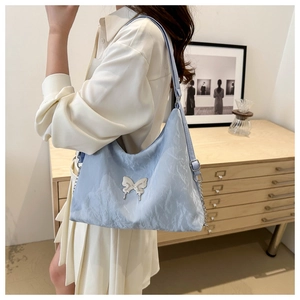 Close-up of light blue pleated shoulder bag with silver butterfly metal detail on a model