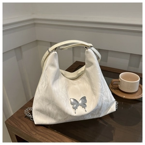 Close-up of cream shoulder bag with wrinkled texture and silver butterfly ornament