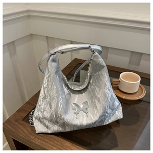 Detail of silver pleated texture handbag with metal butterfly logo on wooden table