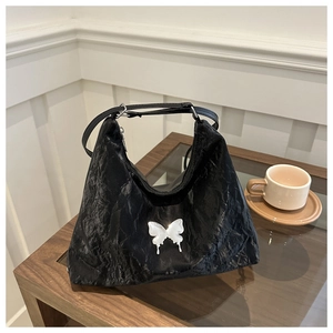 Detail of black pleated shoulder bag with white butterfly charm on a wooden table