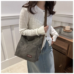 Detail of gray canvas tote bag featuring a leather fashion label and adjustable strap