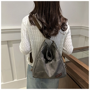 Detail of dark grey canvas backpack with brown leather logo and adjustable straps