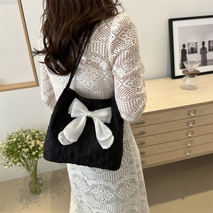 Sac fourre-tout noir avec nœud blanc porté à l'épaule dans un décor intérieur doux