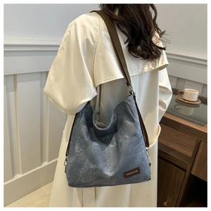 Detail of grey-blue denim crossbody bag with adjustable strap worn by model in white coat