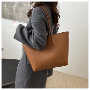 Brown lychee-textured leather tote bag shown on a model wearing a grey wool coat