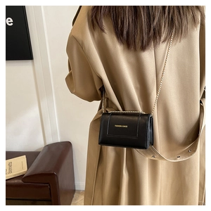 Detail of elegant black square crossbody bag with gold chain strap on beige trench coat