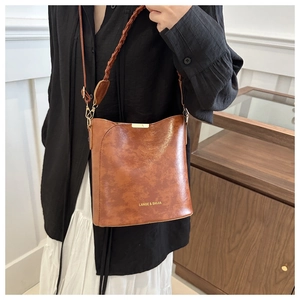 Close-up of vintage brown leather bucket bag with woven strap and gold metal hardware
