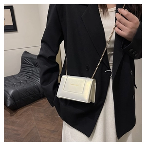 Detail view of pearlescent white crossbody square bag with gold chain strap on a model
