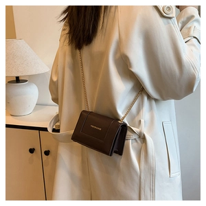 Detail of dark brown chain crossbody bag with golden Fashion & Bags text on beige coat