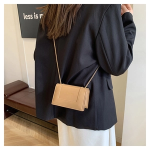 Close-up of beige leather crossbody bag with gold chain strap and fashion text detail
