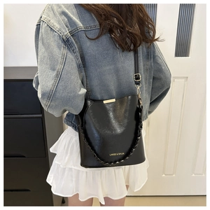 Detail of a black glossy leather bucket bag with gold metal trim and woven handle strap