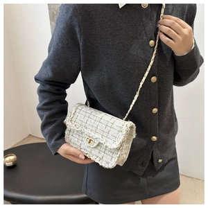 Detail of tweed crossbody bag with gold chain strap and metal turn-lock on a model