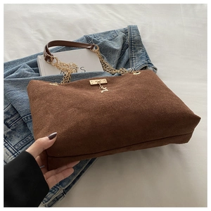 Brown suede tote bag with golden chain strap and deer charm on a soft fabric background