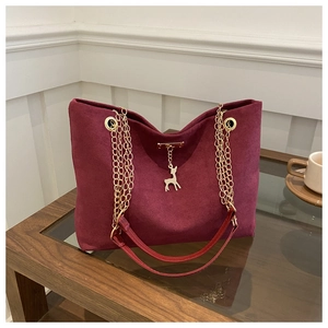 Detail of burgundy suede tote bag featuring a gold chain strap and deer charm