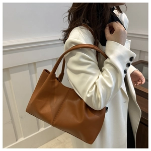 Detailed side view of brown tote bag with pleated bottom design and long handles