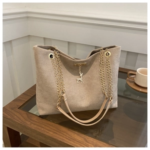 Detail of beige suede tote bag featuring a gold chain strap and deer charm on a table