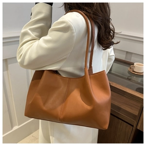 Detailed side view of a large brown leather tote bag worn by a model in a minimalist room