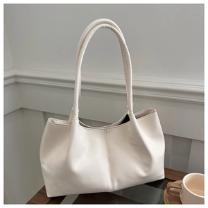 Close-up of cream faux leather tote bag with vertical stitching on a wooden table