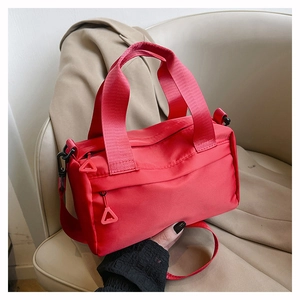 Detail of red nylon shoulder bag featuring wide handles and triangle zipper pull design