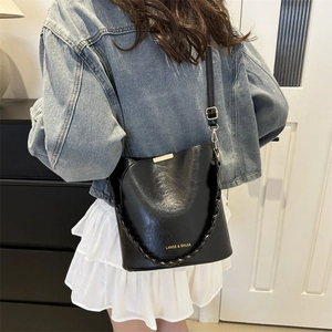 Chic black leather bucket bag with gold hardware and woven handle worn by a model
