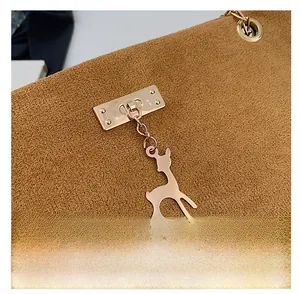 Detail of brown suede shoulder bag with gold metal clasp and deer-shaped pendant charm