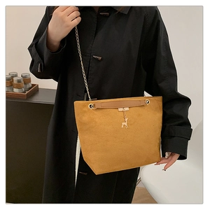 Detail of brown suede tote bag with golden chain strap and deer charm on black coat