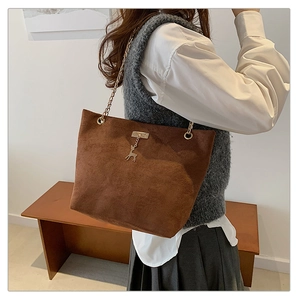 Detail of vintage brown suede tote bag with golden chain strap and deer charm on model