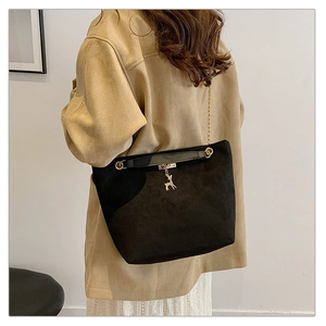 Detail of black suede tote bag with golden chain strap and deer charm on model