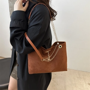 Vintage brown suede tote bag with metal chain strap worn over a black winter coat