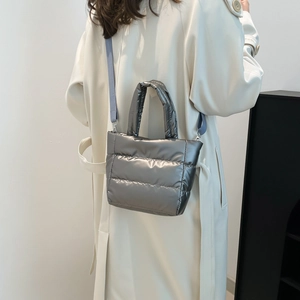 Silver puffer tote bag with quilted padding and adjustable strap worn by model
