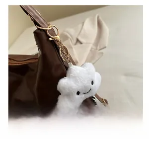 Close-up of white plush cloud keychain with smile embroidery on a brown tote bag