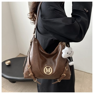 Detail view of large dark brown leather hobo bag with gold M logo and cloud charm