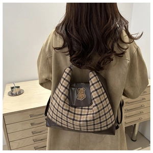 Détail d'un sac à dos vintage à carreaux avec finitions en cuir et écusson d'ours