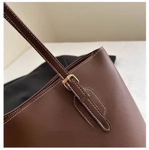 Detail van gouden hardware en wit stiksel op een bruine leren shopper schoudertas