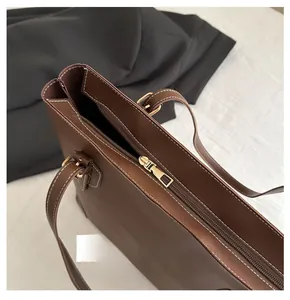 Detail van een donkerbruine lederen tote bag met een gladde goudkleurige metalen rits
