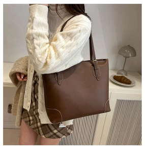 Detail van bruine leren shopper met witte contraststiksels en slanke schouderbanden